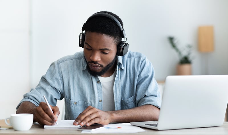 Homme afro-américain rédigeant dans un carnet devant son ordinateur